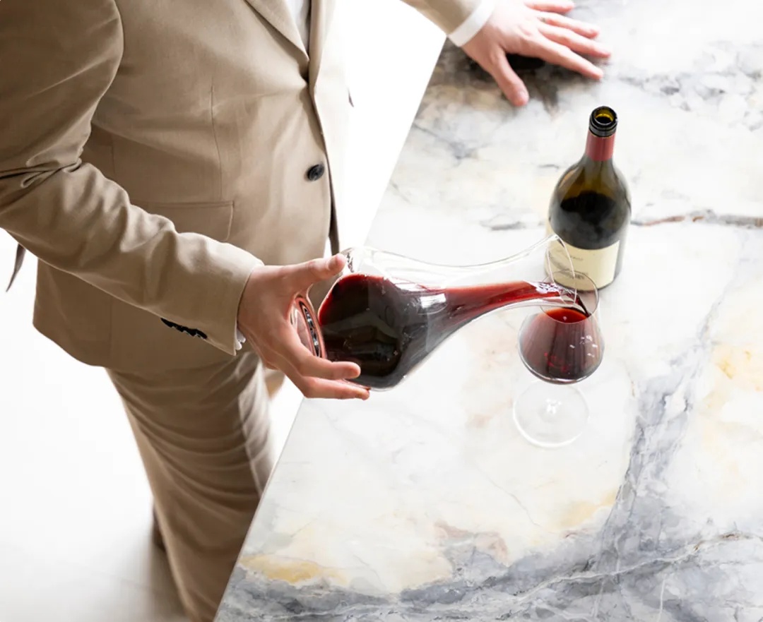 Luxe wijnbeleving: sommelier schenkt rode wijn. Een sommelier schenkt rode wijn uit karaf in glas op marmeren aanrecht.
