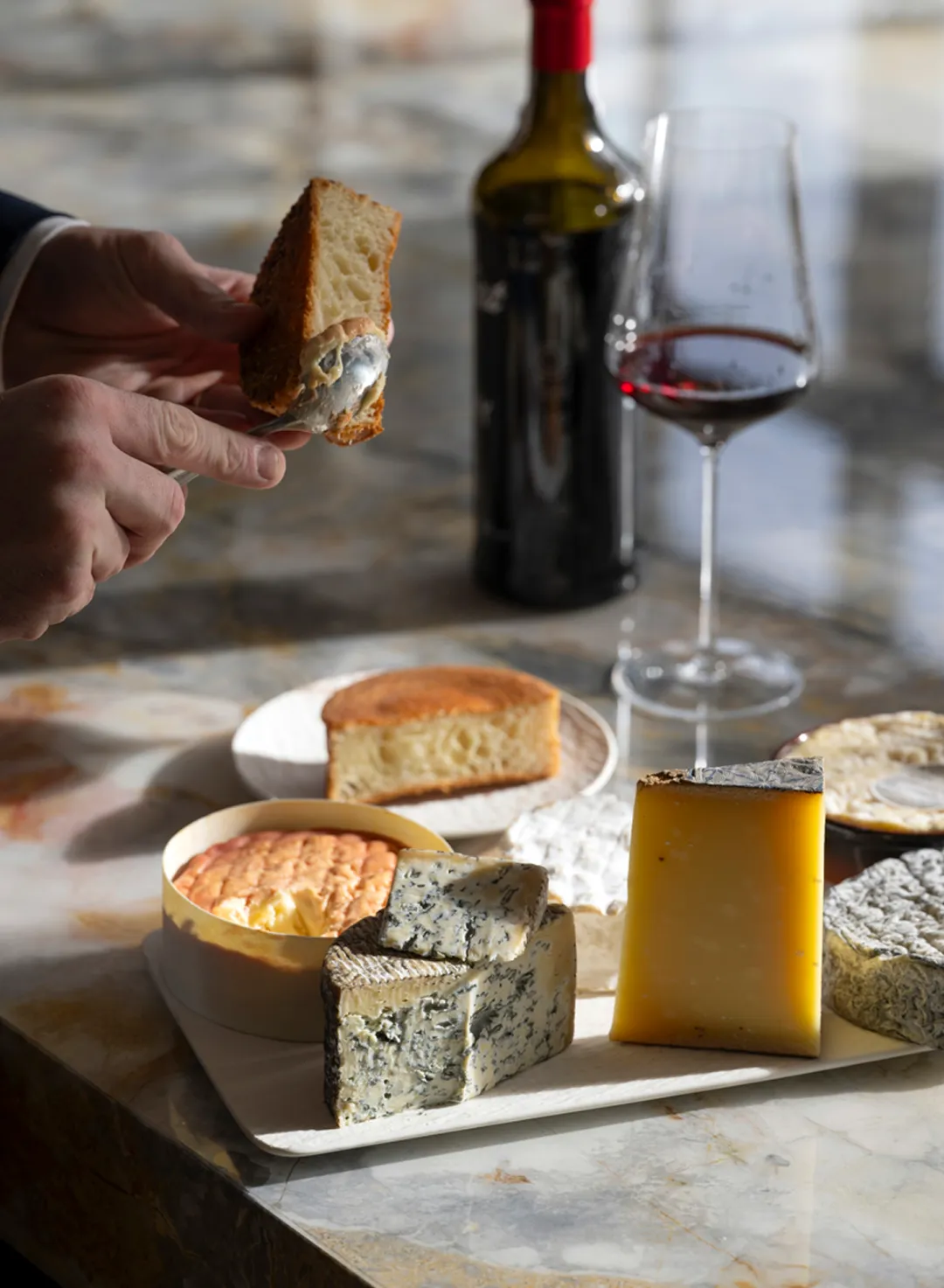 Verfijnde wijndegustatie met kaas Hand schept zachte kaas op brood, met een luxueuze selectie kazen en rode wijn.