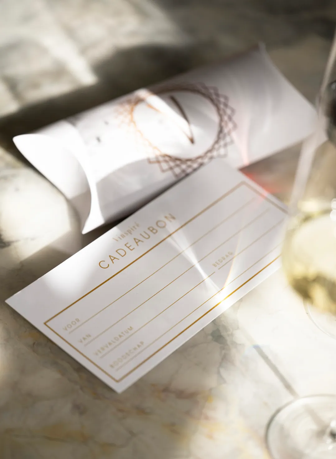 Vinspiré cadeaubon: geef luxe cadeau Witte cadeaubon van Vinspiré met gouden details en een bijpassende geschenkverpakking op marmeren ondergrond.