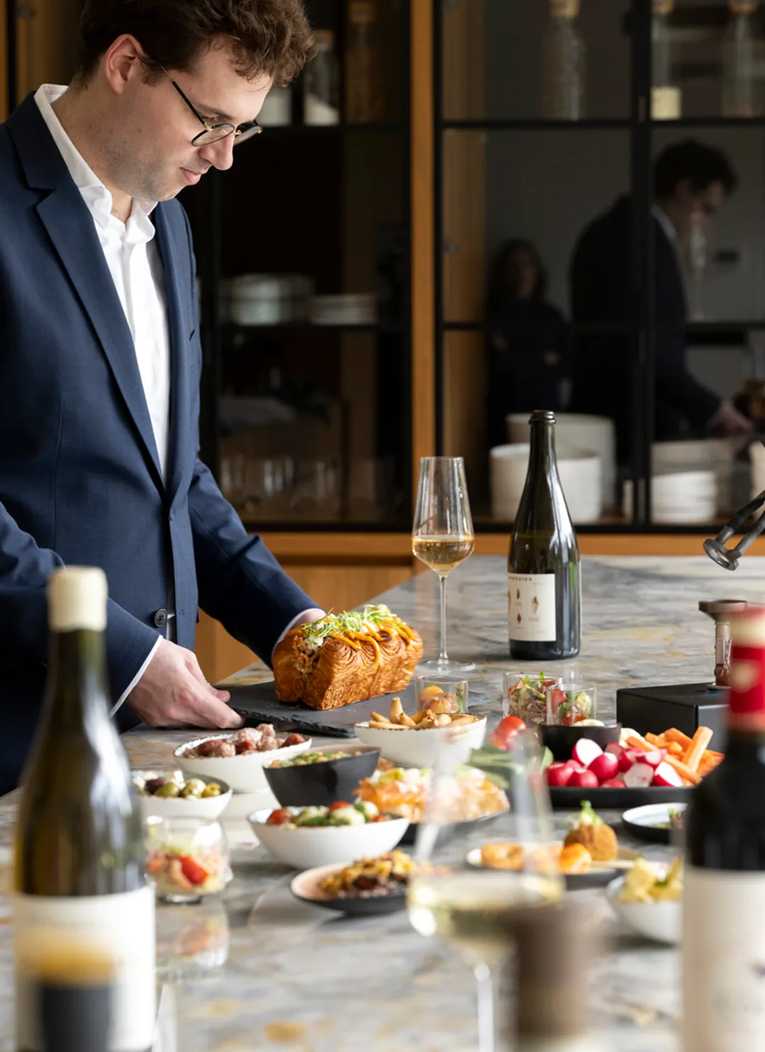 Exclusieve wijnbeleving met culinaire verfijning. Een sommelier plaatst een gevuld bladerdeegbrood op een tafel met premium wijnen en charcuterie.