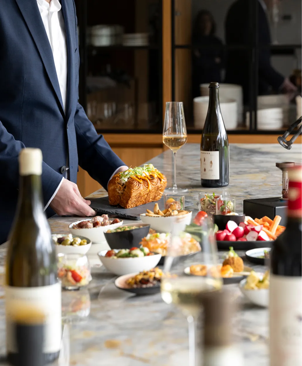 Sommelier in pak serveert gevuld brood bij een tafel vol luxe hapjes en wijnen.