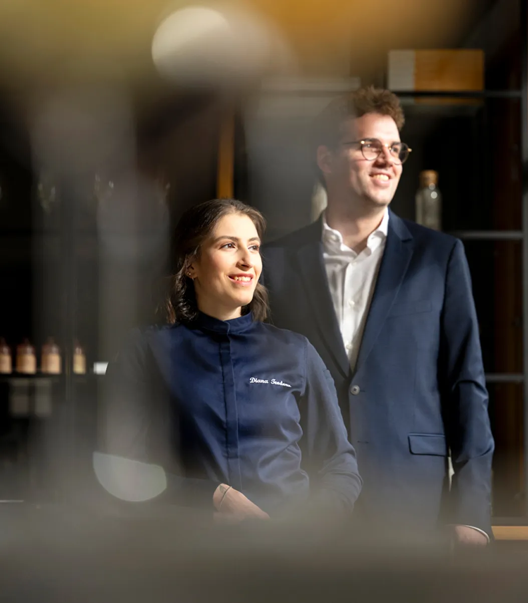 sommelier-patissier-team.jpg Een glimlachende sommelier en patissier staan samen, klaar voor een verfijnde wijnbeleving.